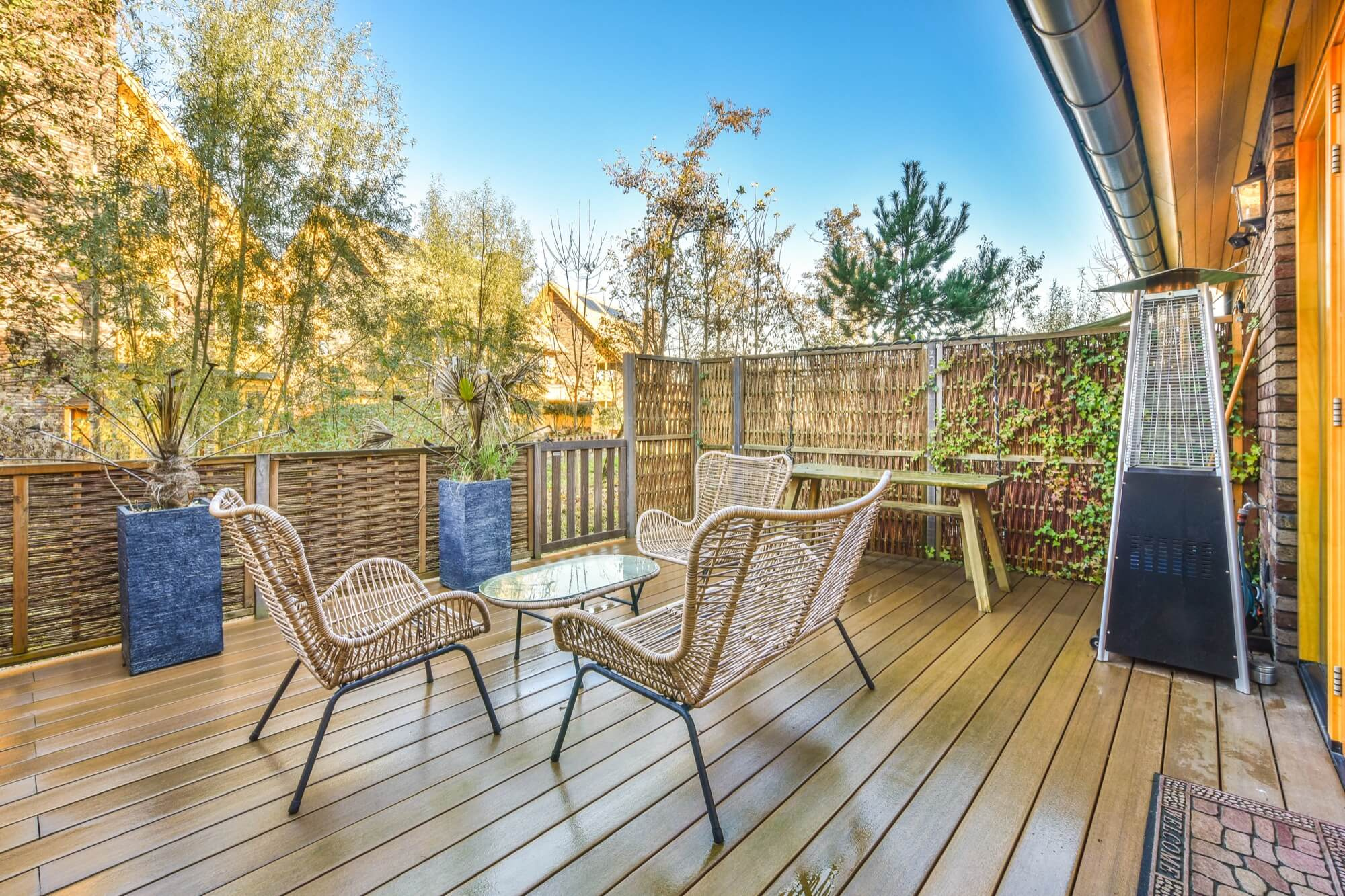 Mysig altan med rottingmöbler, glasbord, bambuskärm och terrassvärmare.