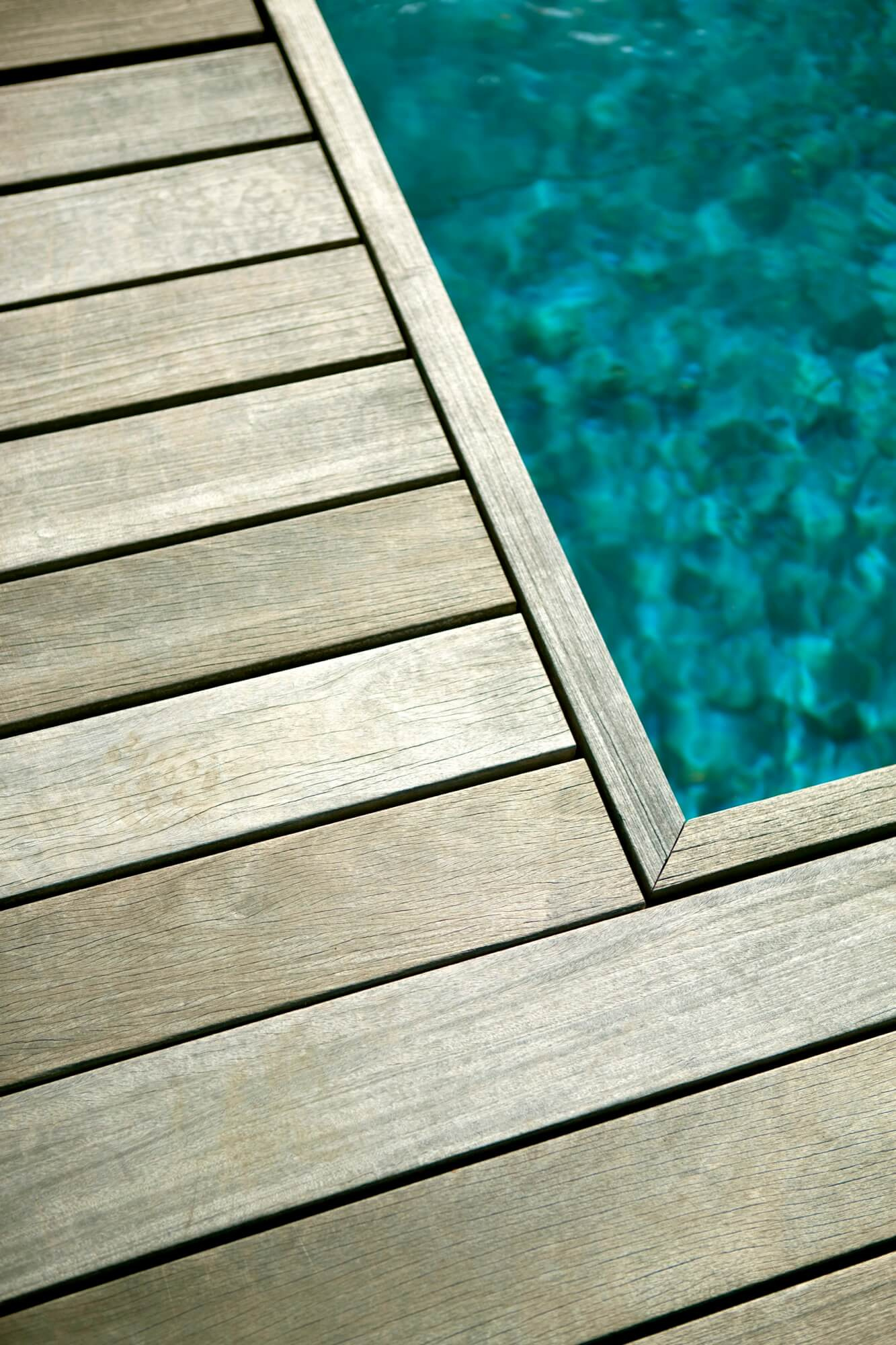 Träaltan vid en pool med klart turkost vatten, närbild på hörn och trall.